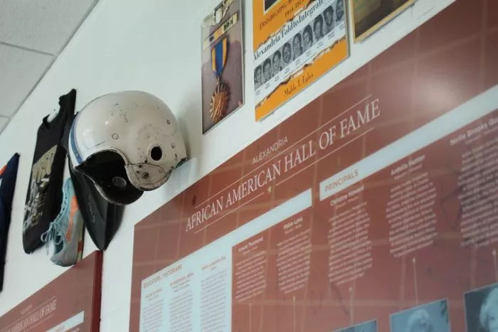 A white helmet hangs on a wall above a large African American Hall of Fame display, surrounded by framed photos, posters, and memorabilia.