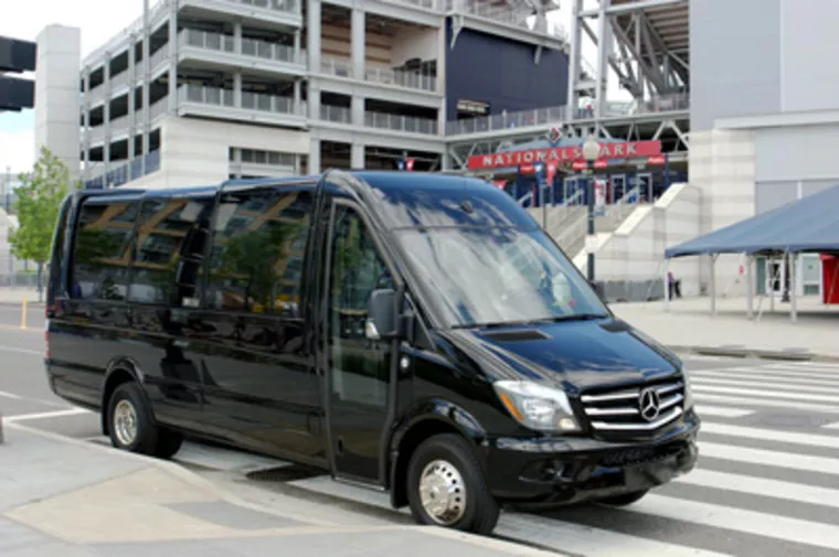 A black Mercedes-Benz Sprinter van is parked on a city street near Nationals Park stadium, with modern buildings visible in the background.