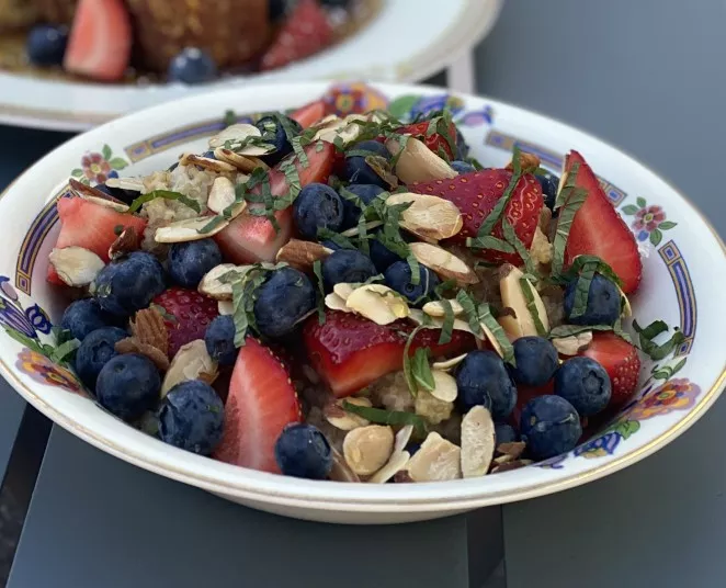 A bowl of oatmeal topped with fresh strawberries, blueberries, sliced almonds, and chopped mint, served in a decorative bowl.