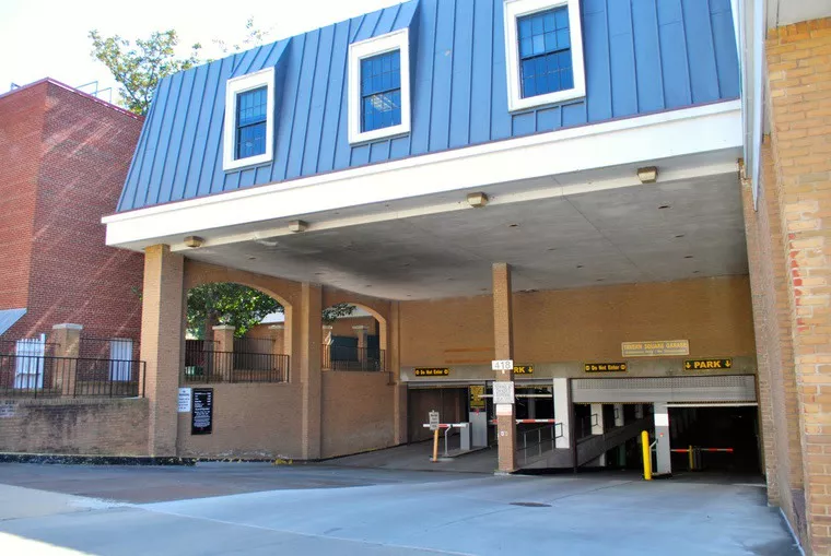 A two-level parking garage entrance beneath a building with brick walls and a blue metal roof, featuring parking signs and clearance bars above the entryways.
