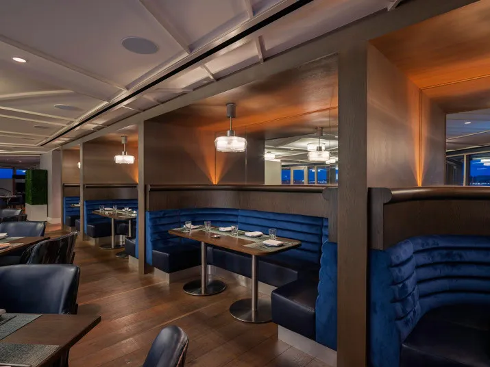 Modern restaurant interior with wooden floors, blue upholstered booth seating, set tables, and soft pendant lighting, creating a cozy and upscale dining atmosphere.