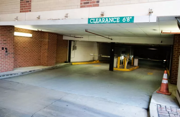 A parking garage entrance with a clearance sign reading CLEARANCE 68. There are orange cones and parking ticket machines visible, with brick walls on either side.