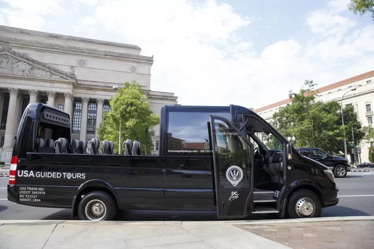 A black USA Guided Tours van with open sides and empty seats is parked on a city street, with historic buildings and green trees visible in the background.