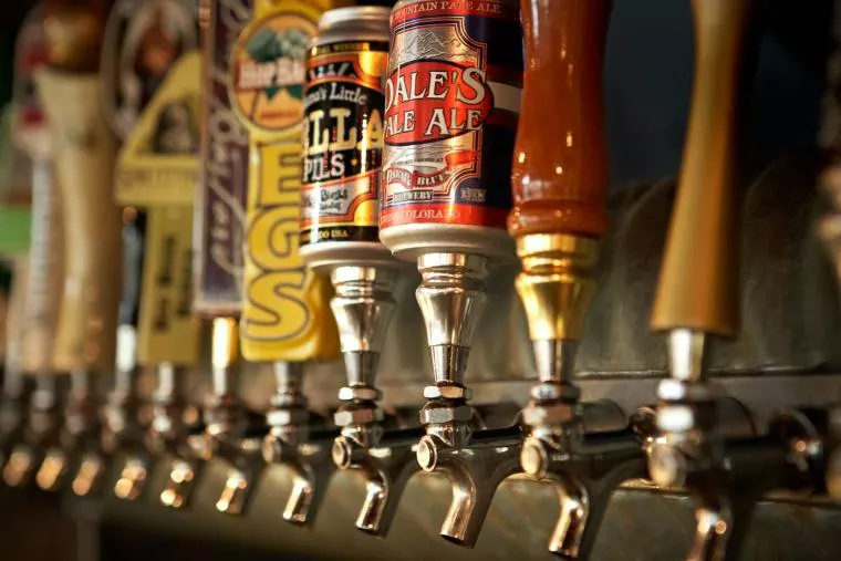 A row of beer taps with colorful handles, each featuring different brands and designs, lined up at a bar, ready to serve draft beer.