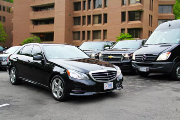 A lineup of black luxury vehicles, including a Mercedes-Benz sedan, a Chevrolet SUV, and a Mercedes-Benz van, parked in front of a modern brick office building.
