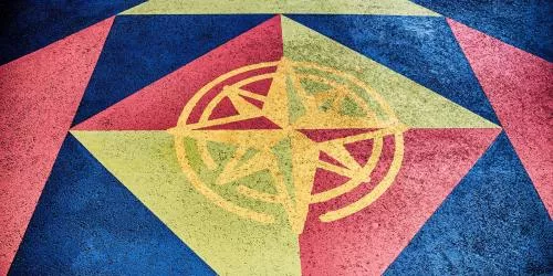 A colorful geometric pattern painted on concrete, featuring a yellow compass rose design at the center, surrounded by blue, red, and yellow triangles and shapes.