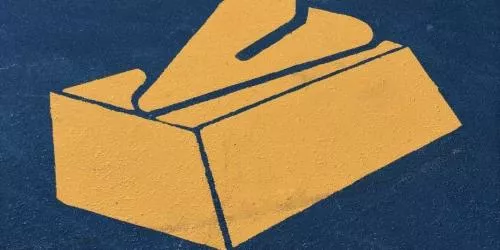 A yellow painted symbol of a tissue box with a tissue coming out, on a dark blue ground.
