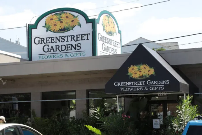 A storefront for Greenstreet Gardens Flowers & Gifts with large signs displaying the store name, featuring sunflower graphics, and surrounded by plants and greenery.