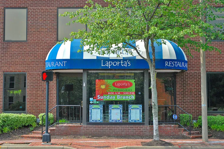 A brick restaurant with a blue and white striped awning labeled “Laporta’s.” Large windows display menus and a colorful sign advertises Sunday Brunch from 10:00 a.m. to 3:00 p.m. A tree grows on the sidewalk in front.