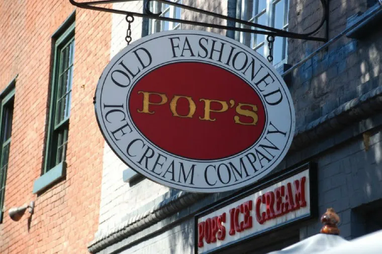 A large oval sign reading POPS OLD FASHIONED ICE CREAM COMPANY hangs outside a brick building above a storefront labeled POPS ICE CREAM.