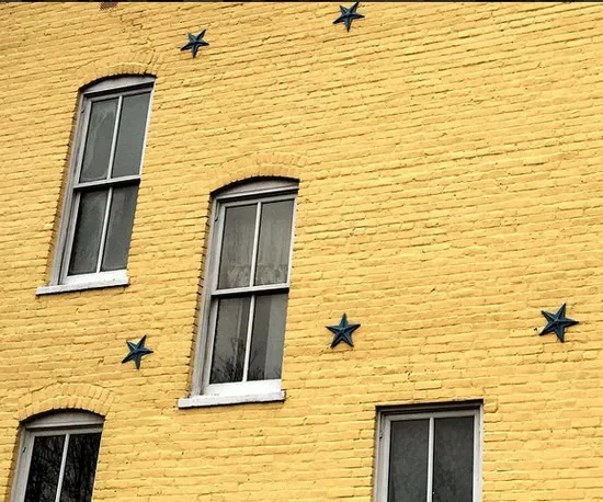 Yellow brick wall with three windows and five blue decorative stars arranged around them. The wall and windows are slightly angled, giving a quirky, offbeat appearance.