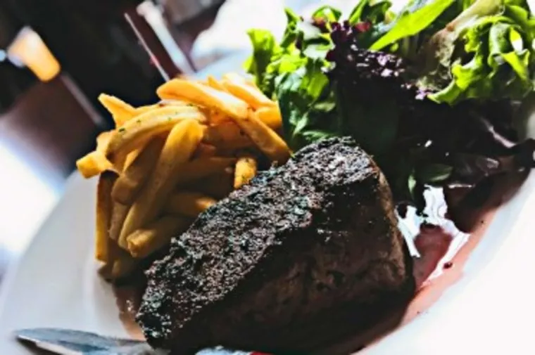 A plate with a grilled steak, a serving of golden French fries, and a fresh green salad, seen in close-up with a knife at the edge of the plate.