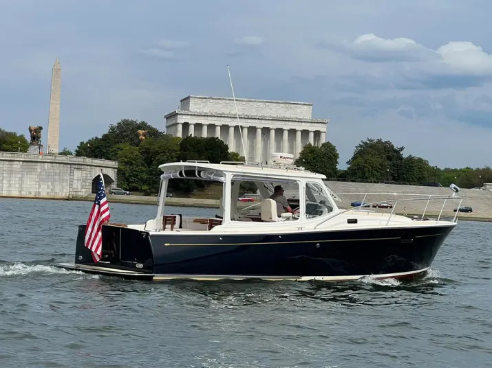 A small motorboat with an American flag cruises on a river in Washington, D.C., with the Lincoln Memorial and Washington Monument visible in the background.