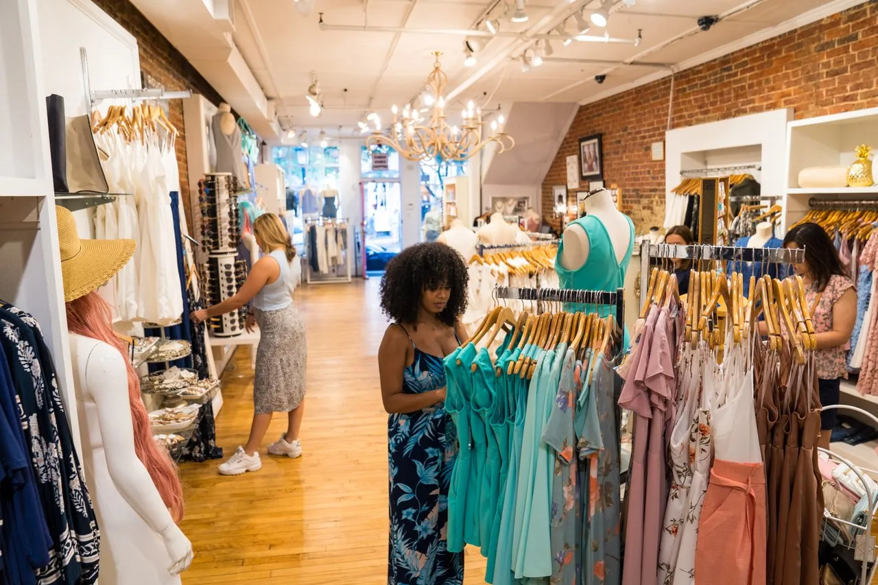 Interior of 3 Sisters Boutique; shoppers look at racks of dresses.