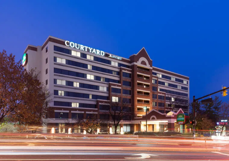 Courtyard by Marriott hotel building at dusk, exterior lights on, with light trails from passing cars in the foreground and trees partially visible on the sides.