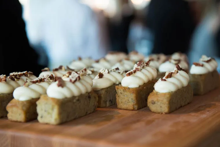 Rectangular mini cakes topped with piped white frosting and sprinkled with chopped nuts, arranged neatly on a wooden board.
