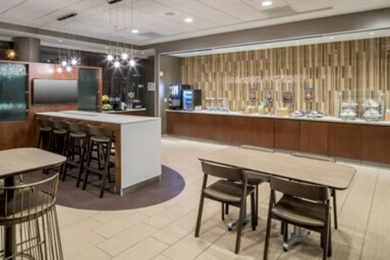 Hotel breakfast area with a buffet counter, stools, dining tables, and chairs.