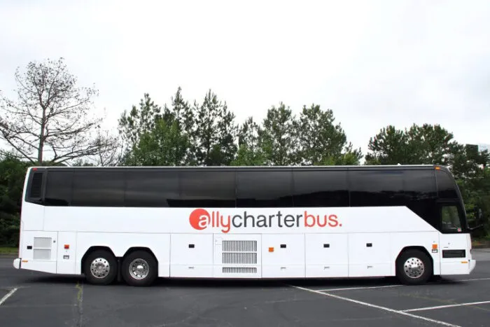 A white charter bus with allycharterbus written on its side, parked in an empty lot with trees in the background.