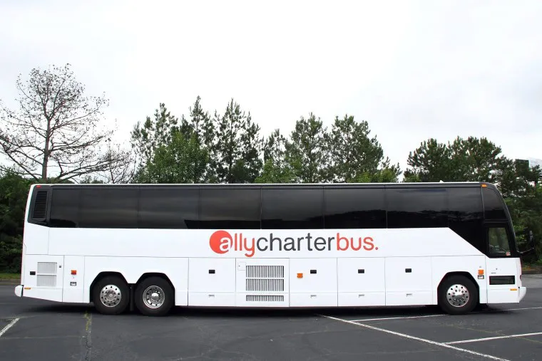 A white charter bus with allycharterbus written on its side, parked in an empty lot with trees in the background.