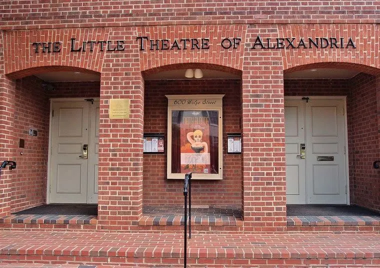 The exterior of The Little Theatre of Alexandria, featuring red brick arches, two white doors, and a poster display in the center above steps. The theater name is displayed above the arches.