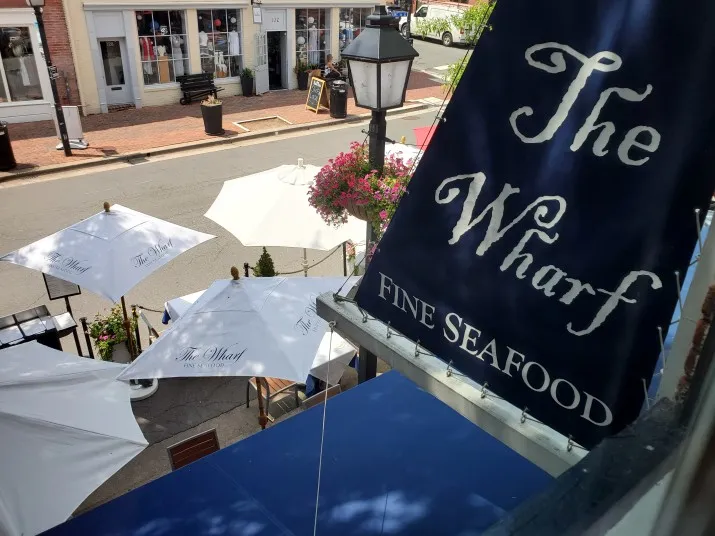 Gemini said Outdoor patio of The Wharf Fine Seafood with white umbrellas and a blue logo banner.
