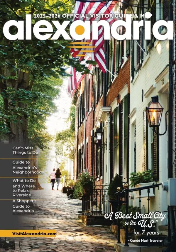 A cobblestone street in Alexandria, Virginia, lined with historic brick row houses, American flags, and greenery, with people walking in the distance under soft sunlight. Text highlights visitor guide topics and city accolades.