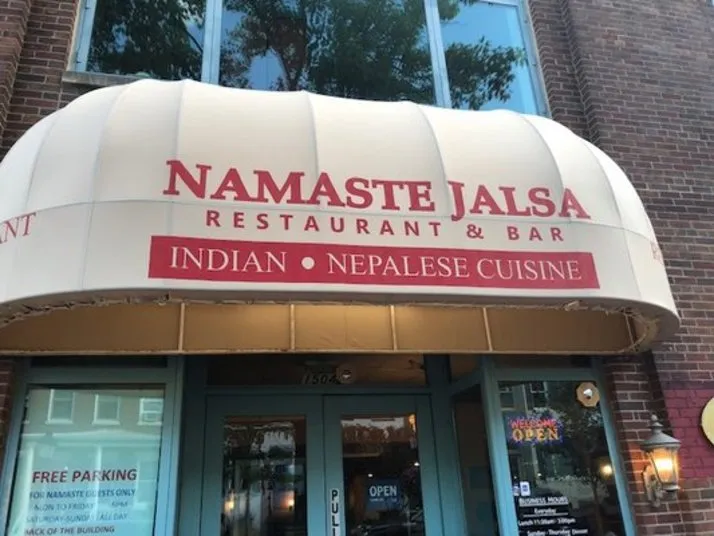 Awning above a restaurant entrance displaying Namaste Jalsa Restaurant & Bar with Indian • Nepalese Cuisine written below; brick building and glass doors are visible underneath.
