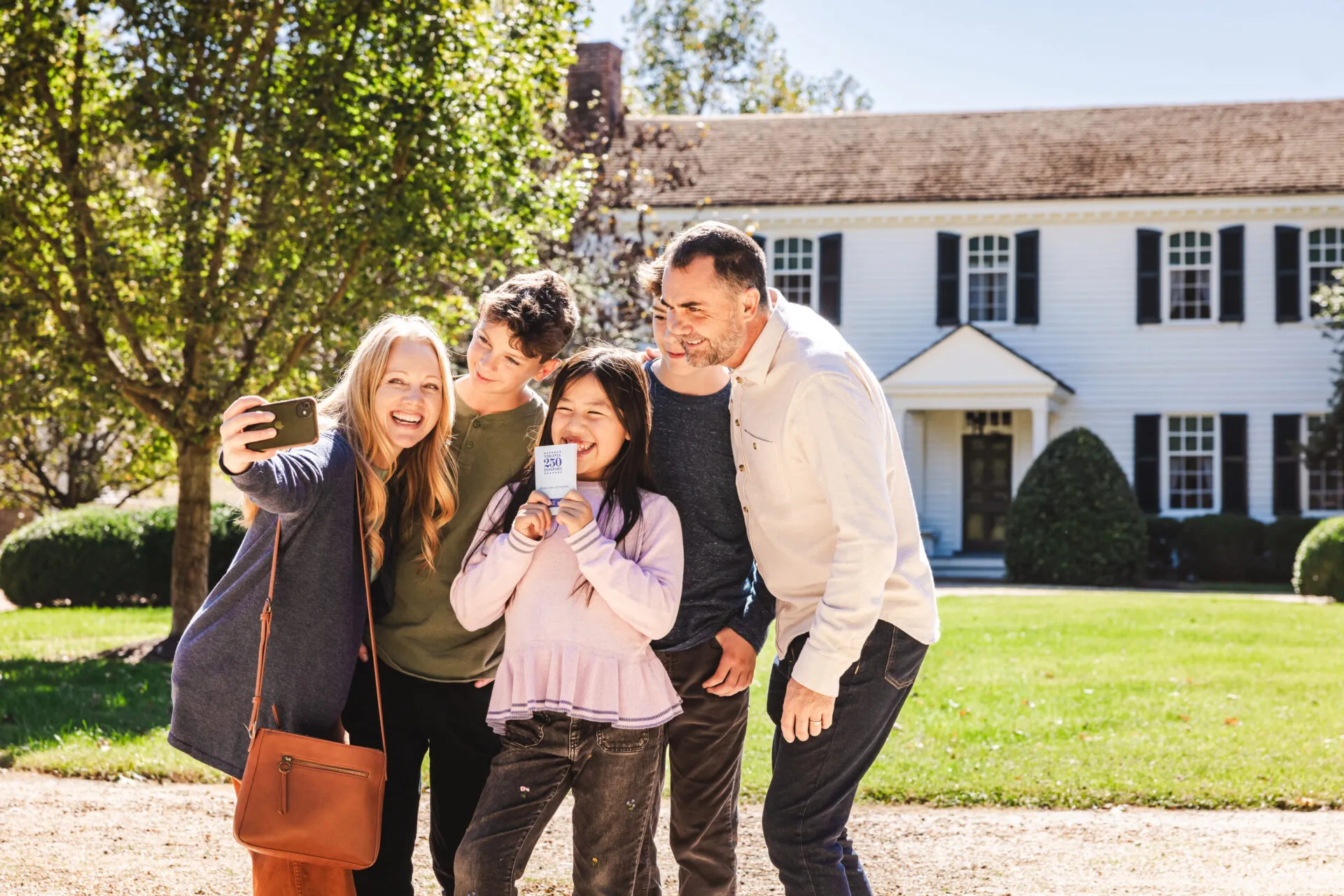 A family takes a selfie with their Virginia 250 passport in front of a historic site.