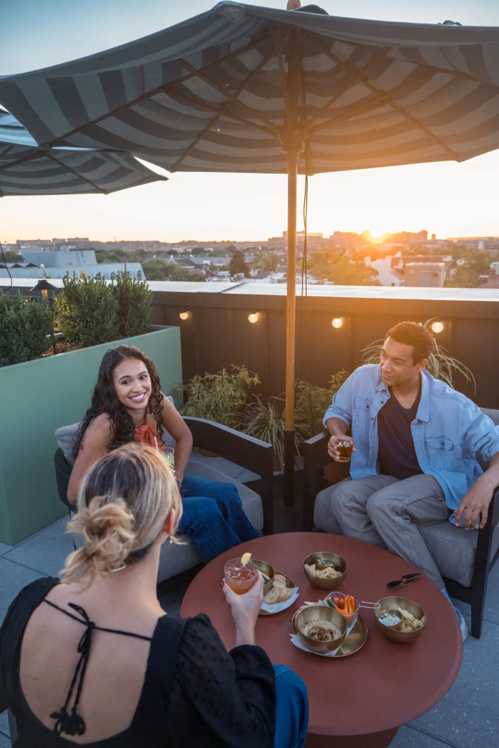Friends enjoying cocktails at an Old Town Alexandria rooftop bar during sunset.