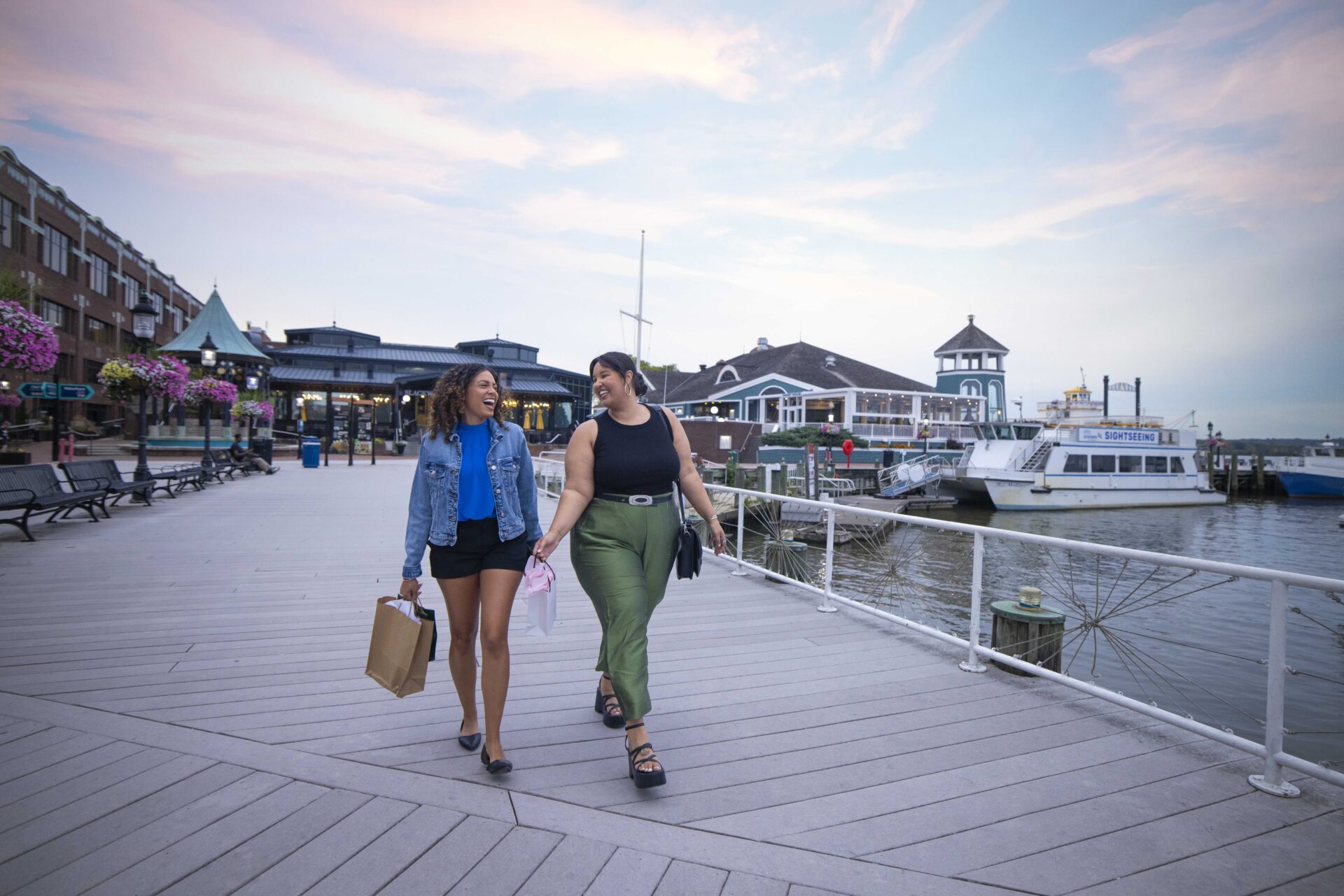 Two young women stroll down a walkway adjacent to the Alexandria waterfront.