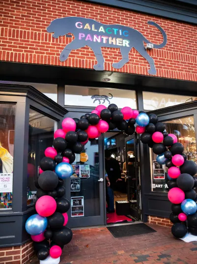 A vibrant black, pink, and blue balloon arch frames the entrance of the Galactic Panther Art Gallery.