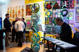 A man playing an electronic marimba at an art gallery event with guests standing in the background.
