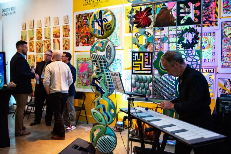 A man playing an electronic marimba at an art gallery event with guests standing in the background.