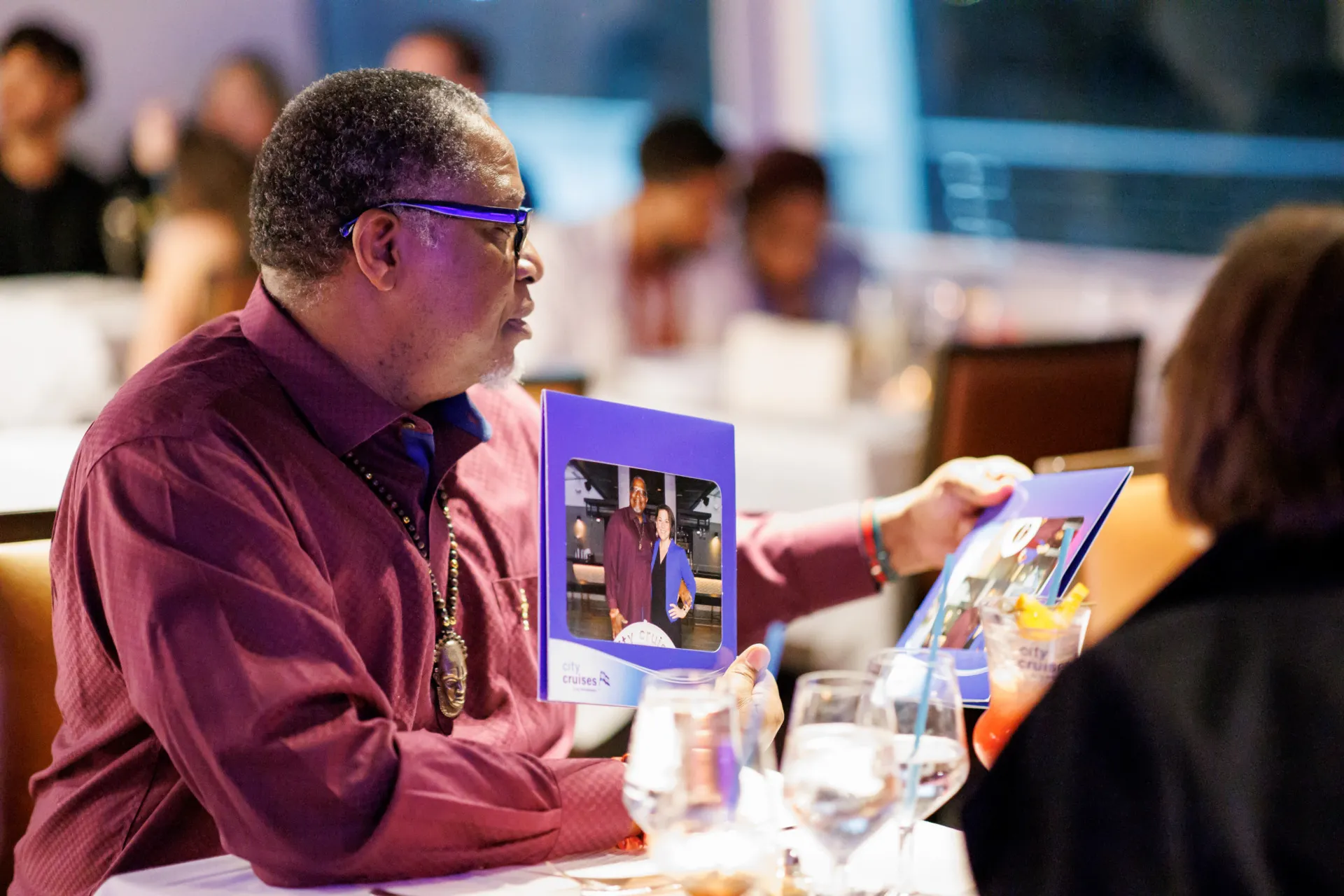A man in a maroon shirt seated at a table on a City Cruises ship, looking at a souvenir photo.