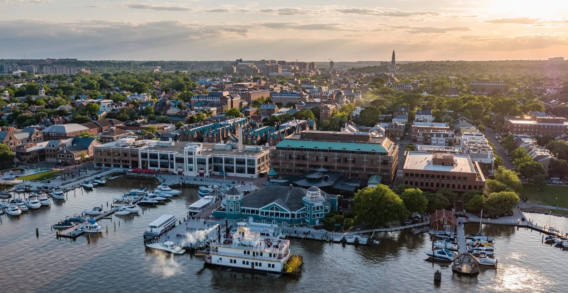 Aerial panoramic view of the Old Town Alexandria waterfront at sunset, featuring the marina, historic buildings, and the Potomac River.