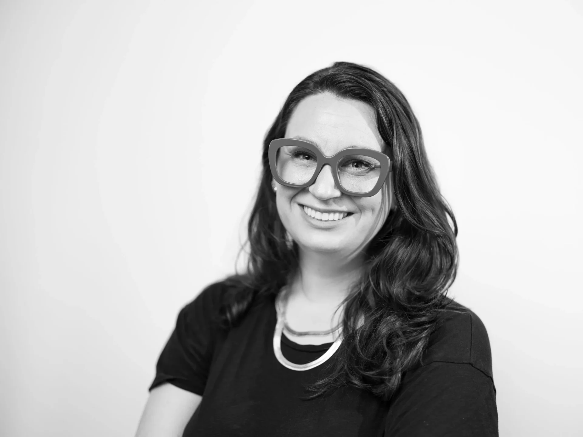 Black and white headshot of Catherine Radachi Chumley smiling and wearing stylish thick glasses.
