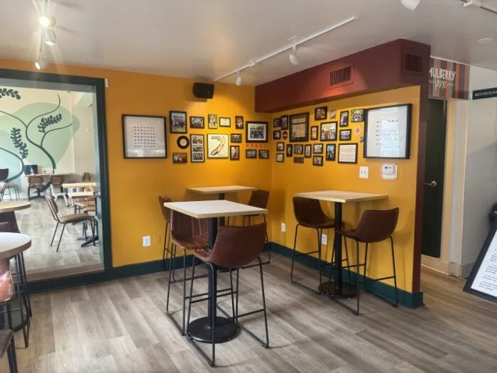Interior of Shorty's Deluxe featuring bright yellow walls, a gallery wall, and bar-height seating.