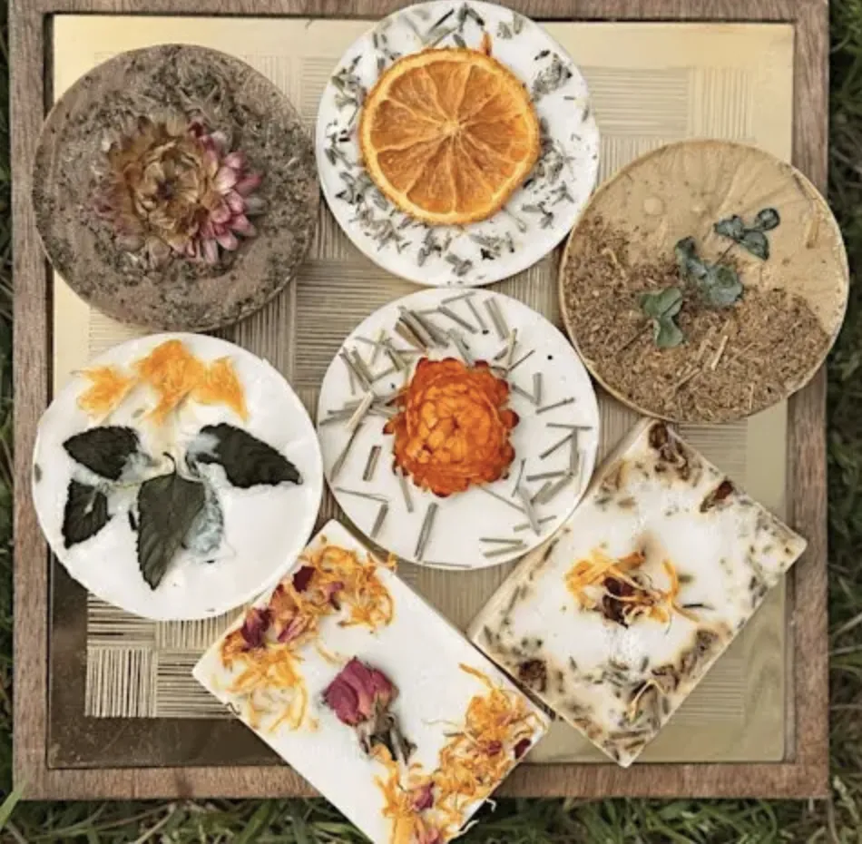 Handmade shea butter soaps decorated with dried orange slices, flowers, and herbs on a tray.