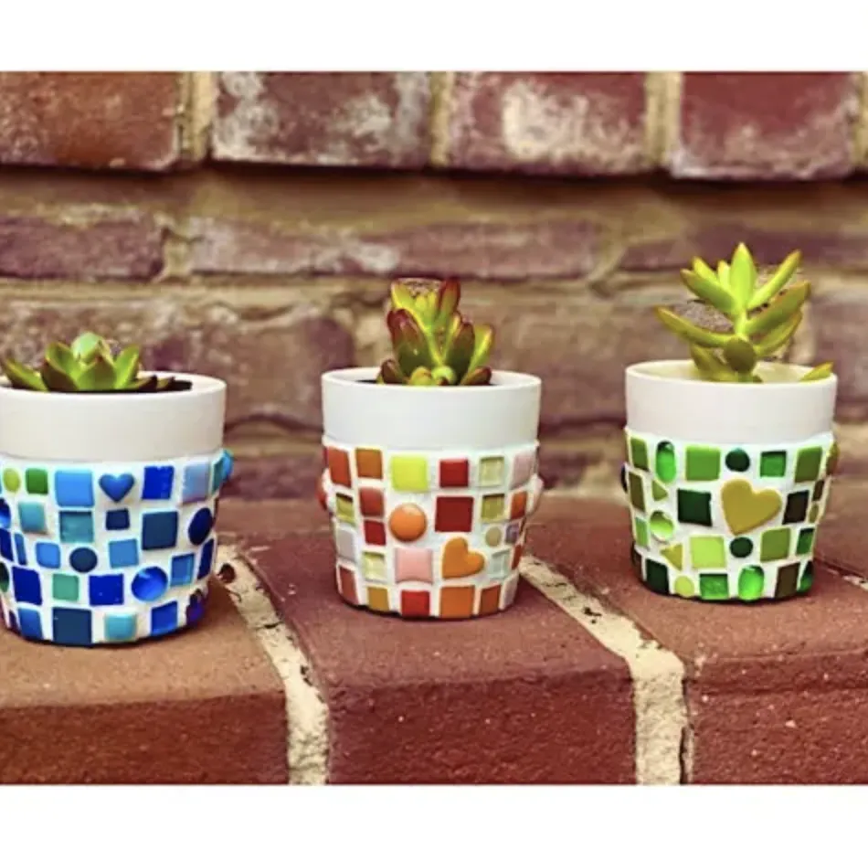 Three small potted succulents in colorful mosaic-patterned mini pots on a brick surface.