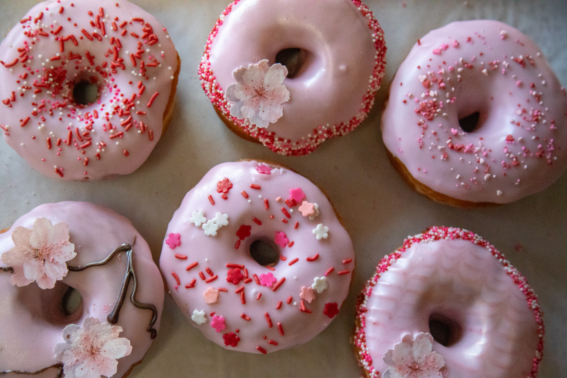 A tray displays six pale pink, beautifully decorated cherry blossom themed donuts from Just Fine Donus in Del Ray.