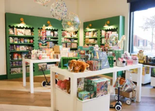 The sales floor as Pippin Toy. Co features colorful and whimsical toys, art supplies, books and more. Built-in shelves line sage green walls, while tables hold merchandise.