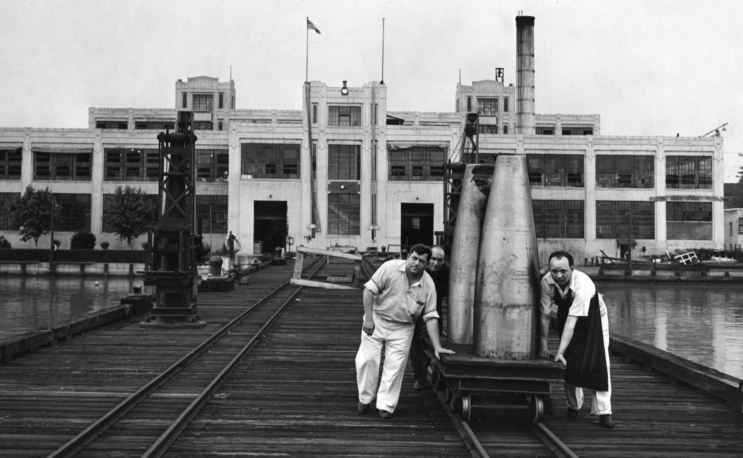 Historical photo of two men moving a torpedo on a cart at the Alexandria Naval Torpedo Station.