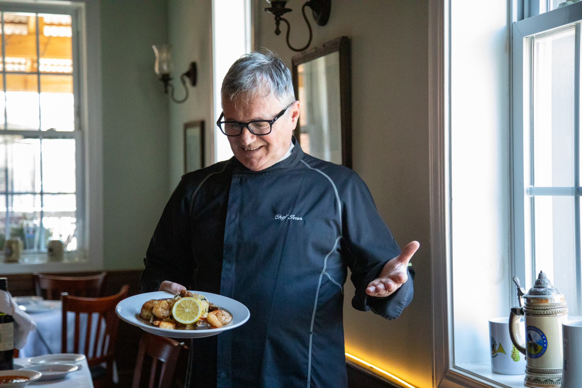 A man in a black chef's shirt holds a plate of food at the Old House Cosmopolitan Grill