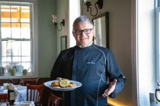 A man in a black chef's shirt holds a plate of food at the Old House Cosmopolitan Grill