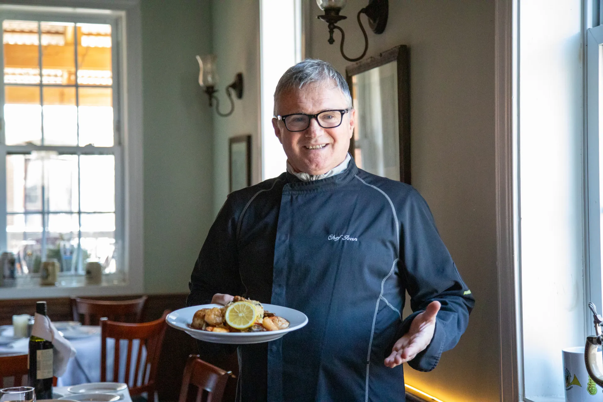 A man in a black chef's shirt holds a plate of food at the Old House Cosmopolitan Grill
