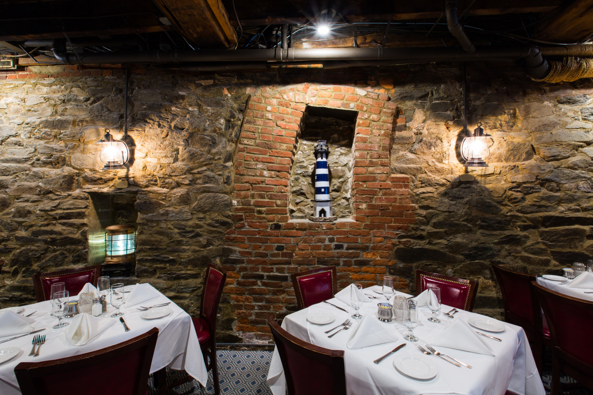 A historic stone wall holds lanterns while tables in the foreground are adorned with crisp white tablecloths.
