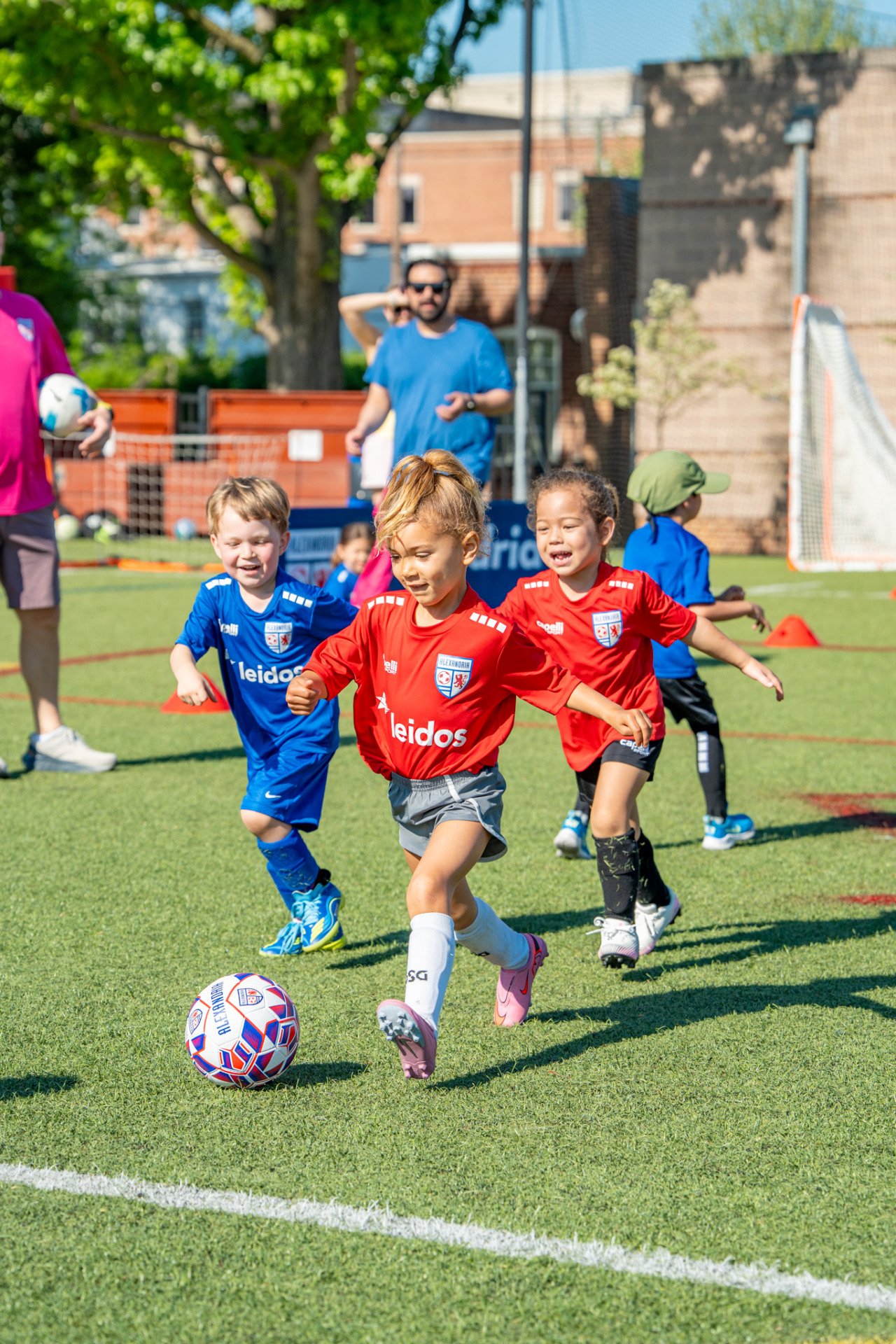 Young children playing a soccer game on a green field during an Alexandria Soccer Association event.