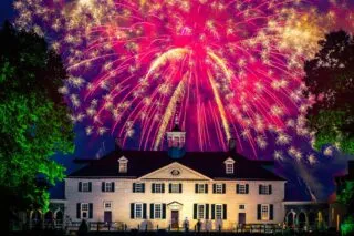 Bright, colorful fireworks exploding over the illuminated historic mansion at George Washington's Mount Vernon.