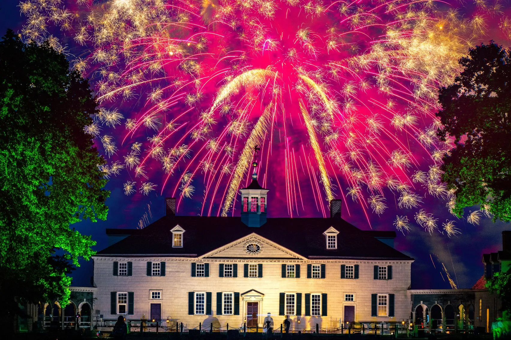Bright, colorful fireworks exploding over the illuminated historic mansion at George Washington's Mount Vernon.