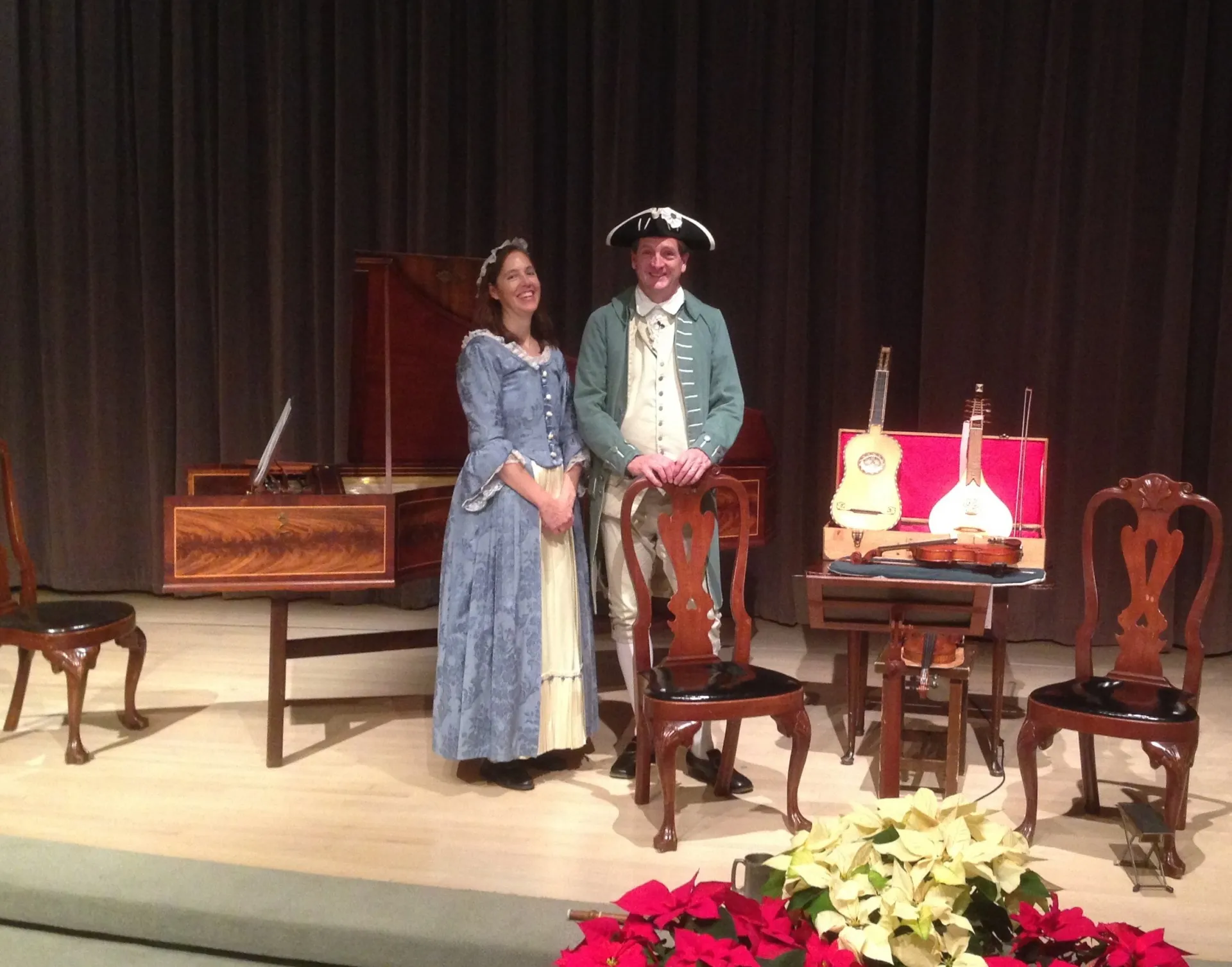 Two musicians in 18th-century attire standing on a stage with historical instruments.